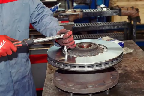 Mechanik w czerwonych rękawicach dokręca śruby podczas wymiany tarcz hamulcowych.