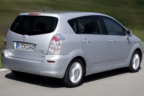 Srebrny Toyota Corolla Verso 2005 jedzie po drodze, w tle zielone wzgórza.