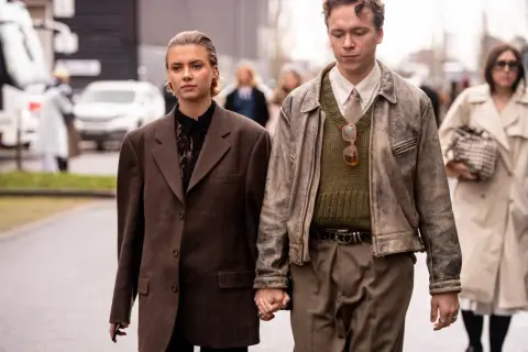 Ein Paar im **Copenhagen Style** geht Händchen haltend. Sie trägt einen braunen Oversize-Blazer, er eine Lederjacke über einem Strickpullover.