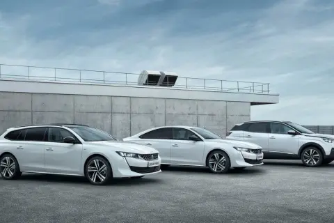 Trzy białe samochody Peugeot 508: kombi, sedan i SUV, stoją przed betonowym budynkiem.