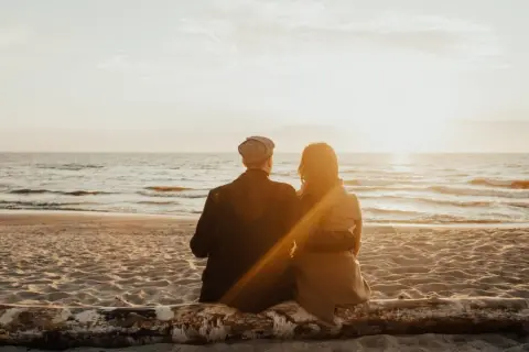 Para dwojga siedząca na pniu na plaży, patrząca na zachód słońca nad morzem. Idealne, fajne miejsce nad morzem dla dwojga.