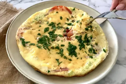 Pyszne śniadanie keto: omlet z pomidorami, serem i natką pietruszki, właśnie nabierany widelcem. Idealny początek dnia.