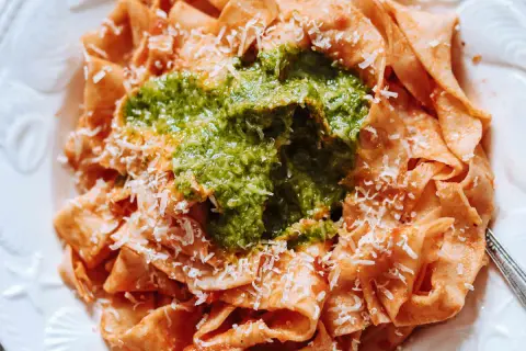 Pappardelle all'arrabbiata z zielonym pesto i parmezanem. Szerokie wstążki makaronu w sosie pomidorowym, przykryte intensywnym, zielonym pesto.