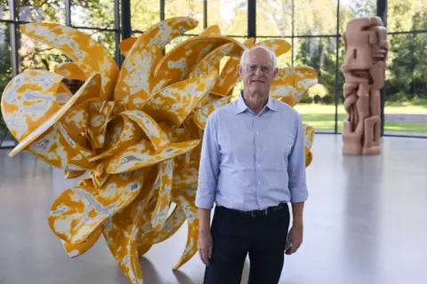 Tony Cragg in Wuppertal vor seiner gelben Skulptur. Im Hintergrund eine weitere Skulptur.