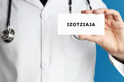 Lekarz w białym kitlu trzyma kartkę z napisem "IZOTZIAJA". Stetoskop wisi na jego szyi.