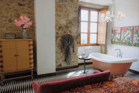 Un bagno rustico chic con vasca freestanding color pesca, pareti in pietra, un accappatoio appeso e un mobile in legno.