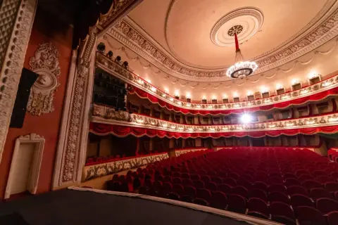Wnętrze teatru z czerwonymi fotelami i bogato zdobionymi lożami. Czekam na pierwszą arię.