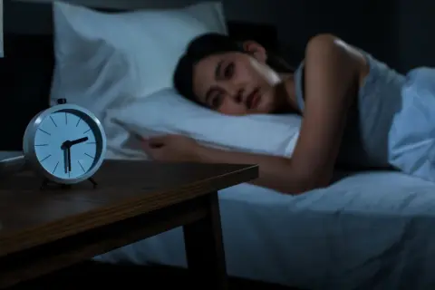 A woman lies awake in bed, staring at the clock. She's trying to figure out how to fall back asleep.