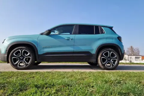 Turkusowy Jeep Avenger na tle błękitnego nieba. Z boku widoczna nazwa modelu i felgi. Idealne wymiary dla miejskiego SUV-a.