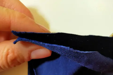 Dłoń trzyma ciemnoniebieską dzianinę welurową z ozdobną lamówką.