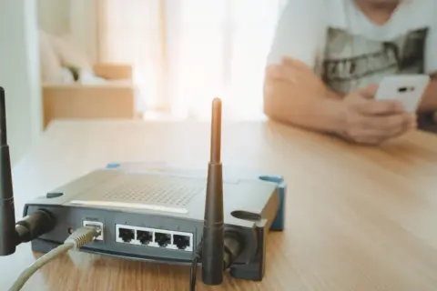 Router z antenkami tworzy domowy hotspot. W tle osoba korzysta z telefonu.