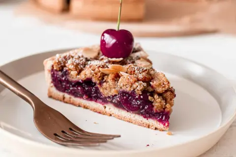 Une part de tarte aux cerises généreuse, garnie d'une cerise fraîche et saupoudrée de sucre glace et d'amandes effilées.
