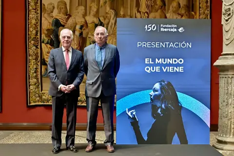 Dos hombres de traje posan ante un cartel de Fundación Ibercaja que anuncia "El mundo que viene", en un evento de martes de libros Ibercaja.