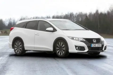 Vit Honda Civic Tourer parkerad på en fuktig väg med träd i bakgrunden.