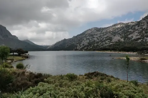 Paisaje sereno de lagos en Mallorca, rodeado de montañas rocosas y vegetación exuberante bajo un cielo nublado.
