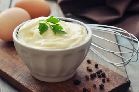 Cremige Mayonnaise ohne Ei, garniert mit Petersilie, neben Eiern und Pfefferkörnern.