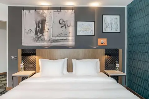 Łóżko w nowoczesnym pokoju hotelowym z białymi pościelami i ozdobami na ścianie.