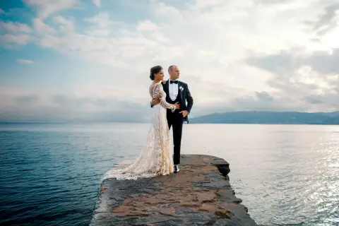 Un couple de jeunes mariés, vêtus de leurs tenues de mariage, pose sur un promontoire rocheux face à la mer. Ces photos de mariage capturent un moment de sérénité.