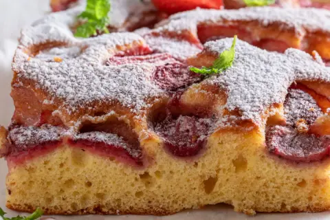 Puszyste ciasto z truskawkami, posypane cukrem pudrem i udekorowane miętą. Idealne na lato, gdy szukasz przepisu na ciasto z truskawkami.