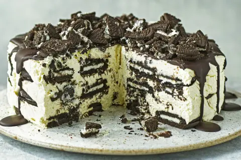 Cremige Oreo Torte mit Schokoladenguss und zerbröselten Keksen obendrauf. Ein Stück ist bereits angeschnitten.