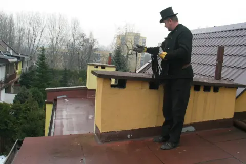 Kominiarz w cylindrze przygotowuje się do przeglądu kominiarskiego, trzymając w rękach liny.