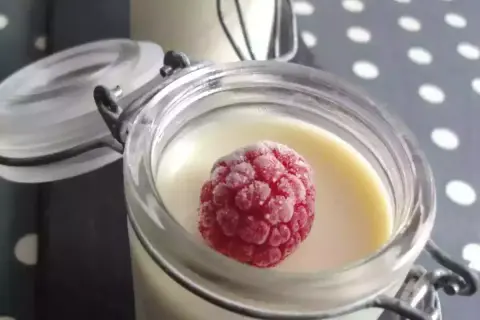 Délicieux panna cotta chocolat blanc, garni d'une framboise givrée, dans un pot en verre.