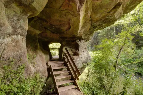 Holztreppe führt aus einer Felsgrotte auf dem schwarzachklamm wanderweg. Ein Fluss plätschert im Hintergrund.
