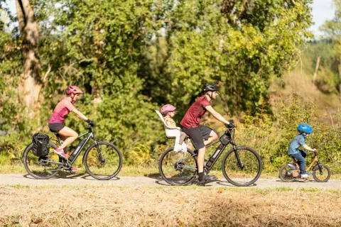 Rodzina na rowerach cieszy się aktywnym wypoczynkiem. Mama z bagażem, tata z córką w foteliku i mały chłopiec na swoim rowerze – idealny przykład turystyki rowerowej.
