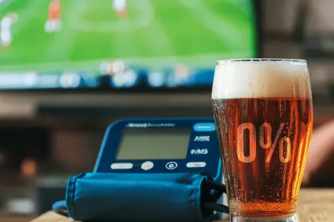 Szklanka piwa 0% i ciśnieniomierz na tle ekranu telewizora.