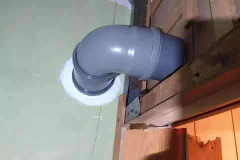 Szary, zakrzywiony kanał wentylacyjny z rury PCV, zamontowany w ścianie, stanowi element wentylacji grawitacyjnej.