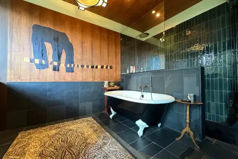 Salle de bain moderne avec baignoire sur pieds noire, tapis persan et mur boisé orné d'une œuvre d'art abstraite. Une **rénovation baignoire** réussie.