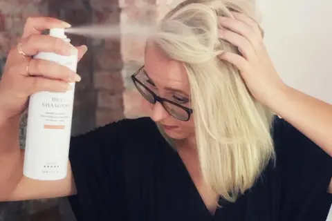 Kvinna med blont hår sliter torrschampo i håret för volym och textur.