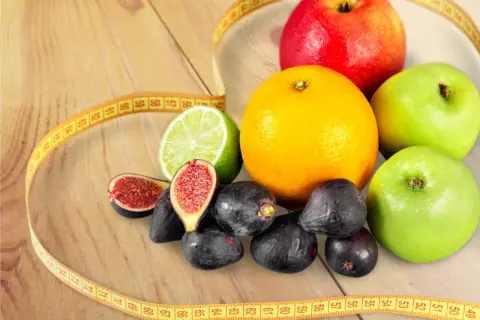 Jabłka, pomarańcza, figi, limonka i miarka krawiecka – idealne owoce na diecie.