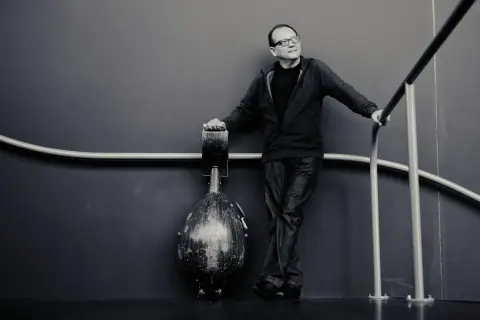 Anouar Brahem, w okularach, opiera się o poręcz, obok niego stoi instrument.