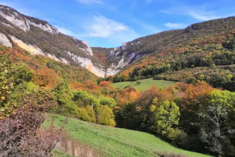 Vallée automnale aux couleurs vives, menant à la cascade de Chaudeyrolles. Le ciel bleu contraste avec les falaises et les arbres aux teintes orangées et vertes.