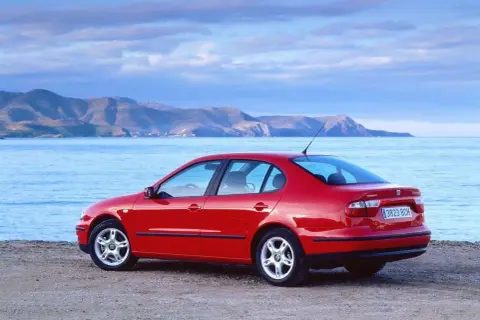 Czerwony Seat Toledo 2 na plaży, z widokiem na morze i góry w tle. Idealny na wakacyjną podróż.