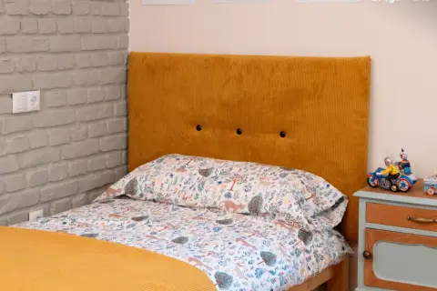 Cabecero tapizado en pana mostaza, ideal para aprender como tapizar un cabecero. Cama con ropa de cama infantil y mesita de noche.