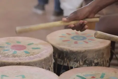 Mani che percuotono tamburi decorati con motivi solari, creando la vibrante musica africana.