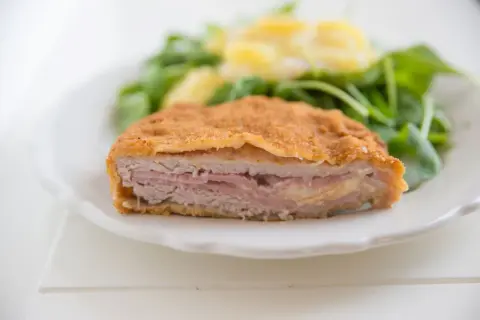 Schab po szwajcarsku, panierowany kotlet z szynką i serem, podany z sałatką.
