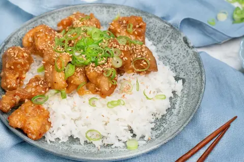 Krispig orange chicken med sesamfrön och salladslök serveras på en bädd av vitt ris. En läcker asiatisk rätt.