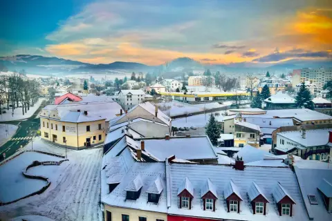 Zimowy krajobraz miasta w Czechach blisko granicy. Śnieg pokrywa dachy i ulice, a w oddali widać wzgórza.