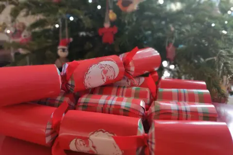 Boże Narodzenie w Wielkiej Brytanii tradycje: czerwone świąteczne petardy z Mikołajem i w kratkę, w tle choinka.