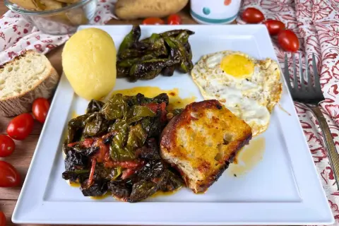 Piatto con friggitelli in padella, uovo fritto, patata lessa, pane tostato e pomodorini.