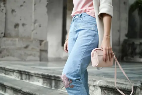 Frau in Jeans mit Blumenstickerei und rosa Tasche. Ein Symbol für die Probleme von Fast Fashion, die oft auf Kosten von Mensch und Umwelt gehen.