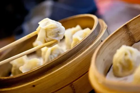 Dampfende Dumplings werden mit Stäbchen aus einem Bambuskorb gehoben. Ein köstliches Dumplings Rezept zum Nachmachen.