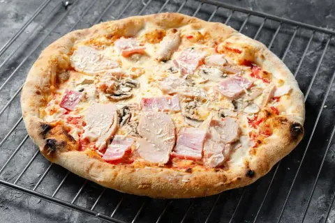 Eine knusprige Pizza mit Schinken und Pilzen auf einem Gitterrost.