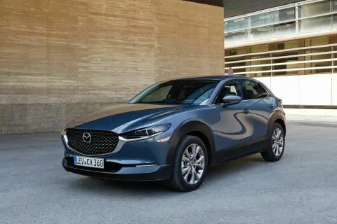 Elegancka Mazda CX-30 w szarym kolorze, zaparkowana przy nowoczesnym budynku. Choć auto prezentuje się świetnie, warto pamiętać o potencjalnych wadach Mazdy CX-30.
