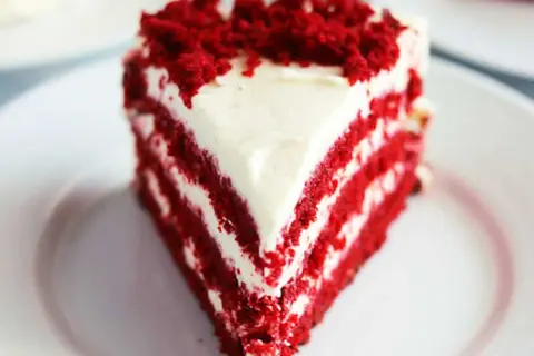 En saftig bit red velvet cake med fluffig frosting och smulor på toppen.