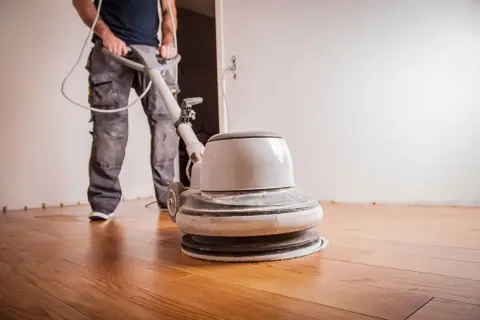 Un ouvrier utilise une ponceuse pour appliquer de l'huile sur un parquet en bois.