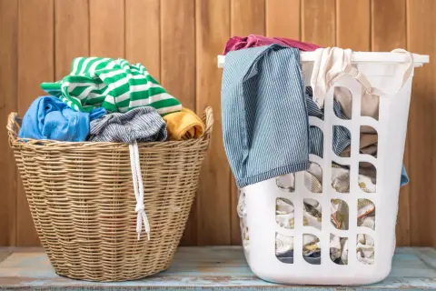 Zwei Wäschekörbe, einer aus Weide, der andere weiß, gefüllt mit Kleidung. Grüne und weiße Streifen, Blau und Gelb. Die Frage ist, welche Farben zusammen waschen.